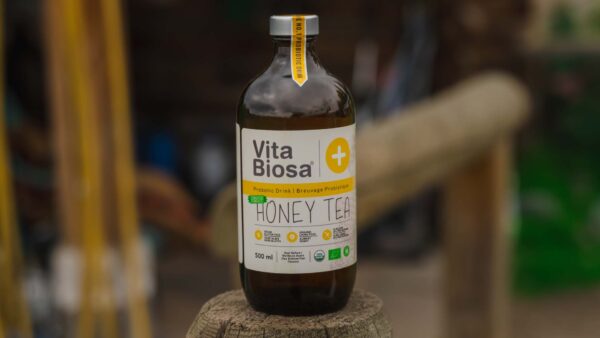 Bottle of Vita Biosa Honey Tea surrounded by tea leaves and honeycomb, highlighting its natural ingredients and refreshing appeal.